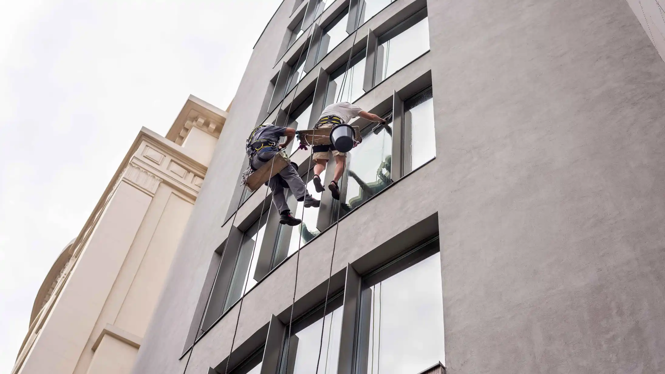 two-workers-washing-windows-outside-building servicio de hidrolavado de grandes estructuras