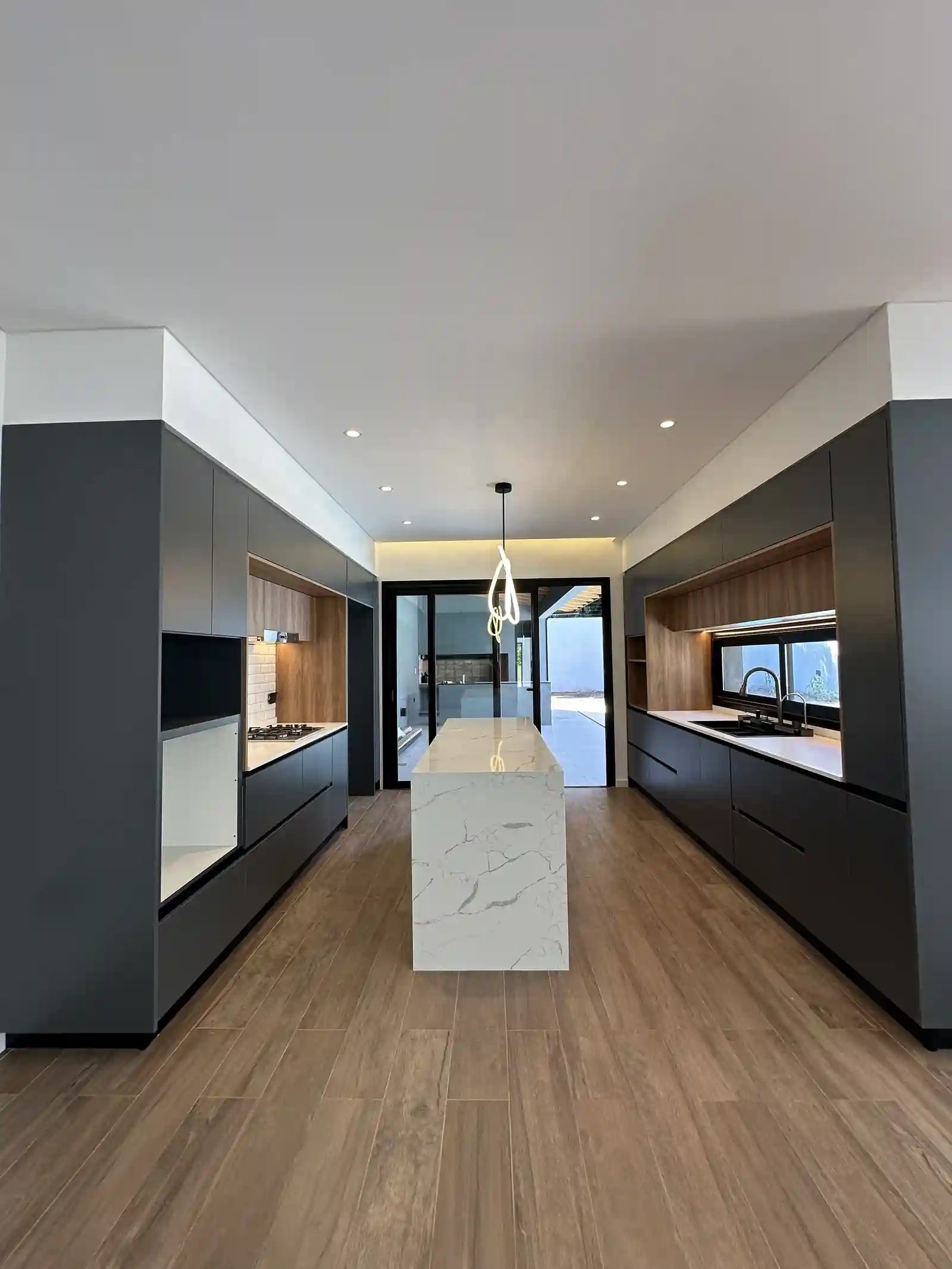 Cocina de Casa Adrogué abierta hacia el comedor, con isla de cuarzo y frentes en grafito y madera