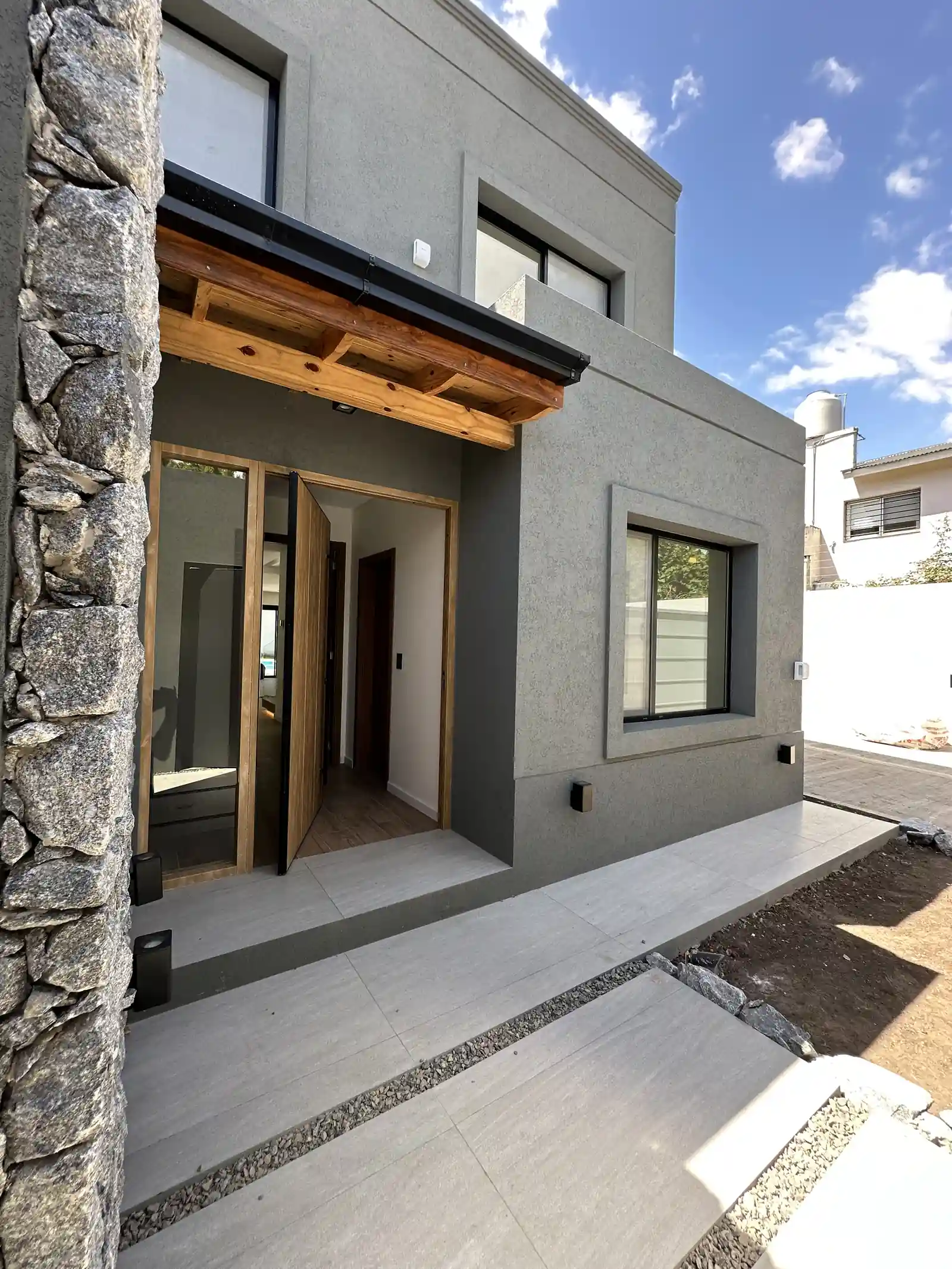 Acceso de Casa Adrogué con muro de piedra, madera y hormigón